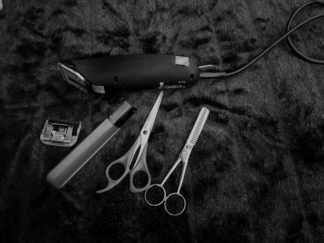 Clippers, scissors and comb laid out on a black cloth