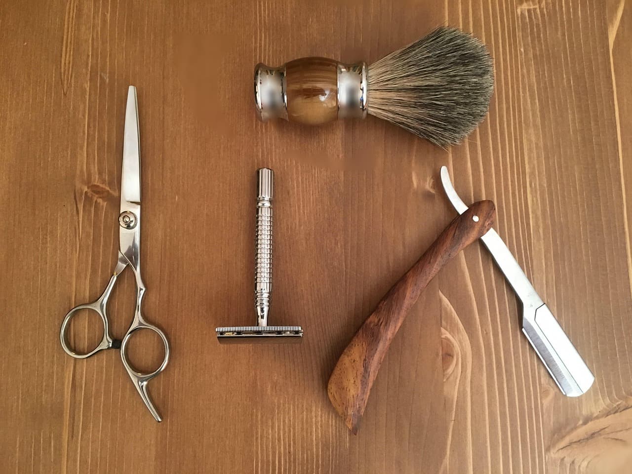 Scissors, razor and shaving brush laid out on a wooden counter